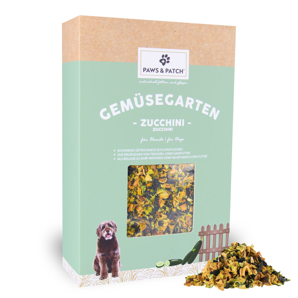 Hellgründe Verpackung aus Pappe mit Sichtfenster, das Zuchhiniflocken zeigt - davor ein Häufchen ausgepackte Zucchiniflocken